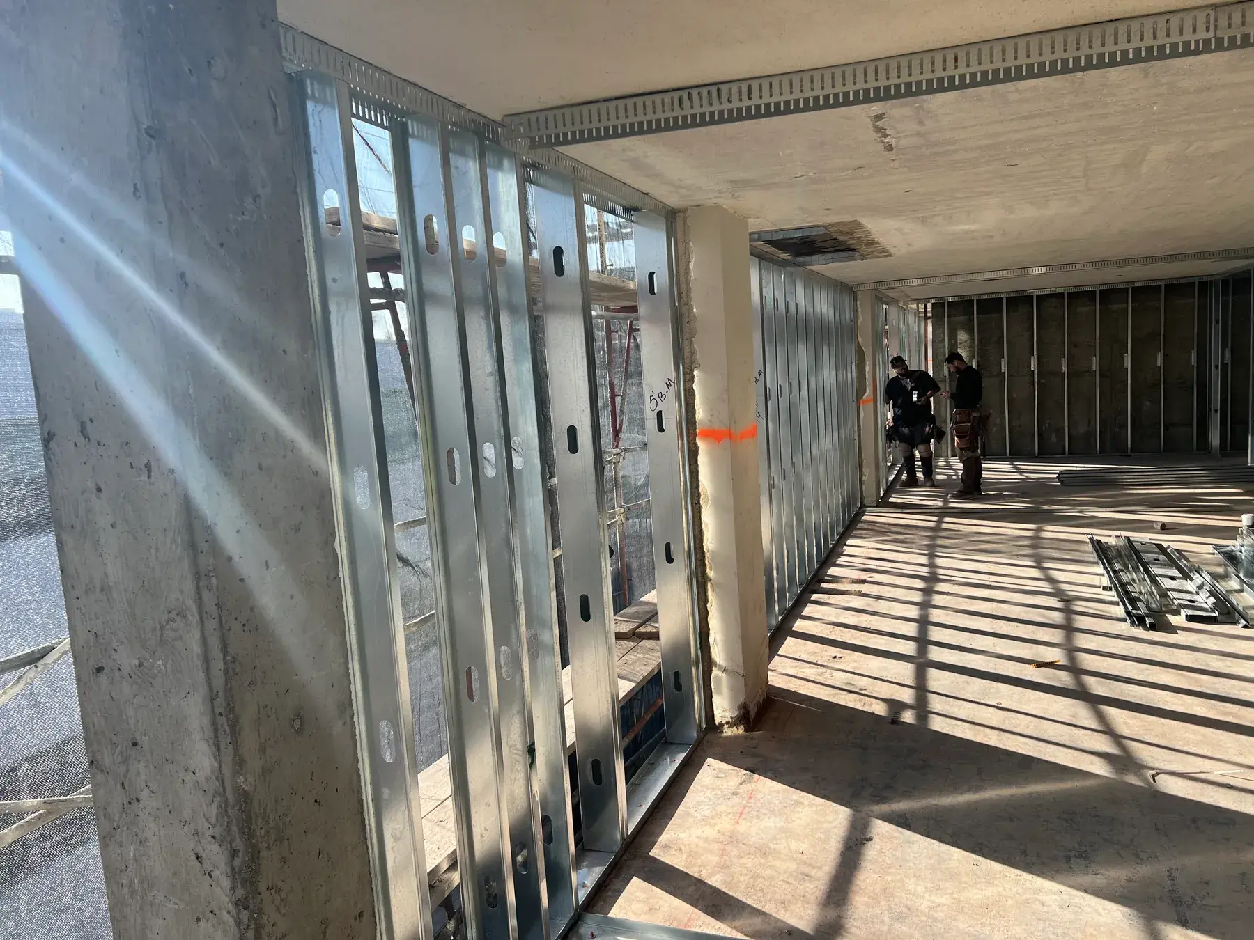 Metal stud corridor walls framed along a concrete deck, with two framers working at the far end
