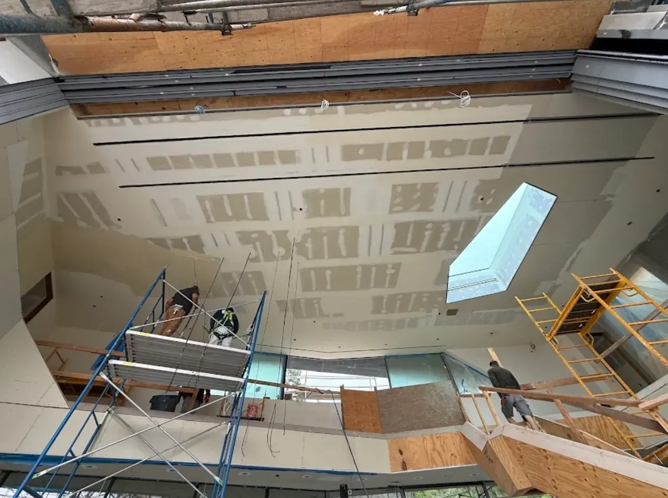 Crew finishing a tall vaulted ceiling from scaffold, with a skylight framed into the drywall above