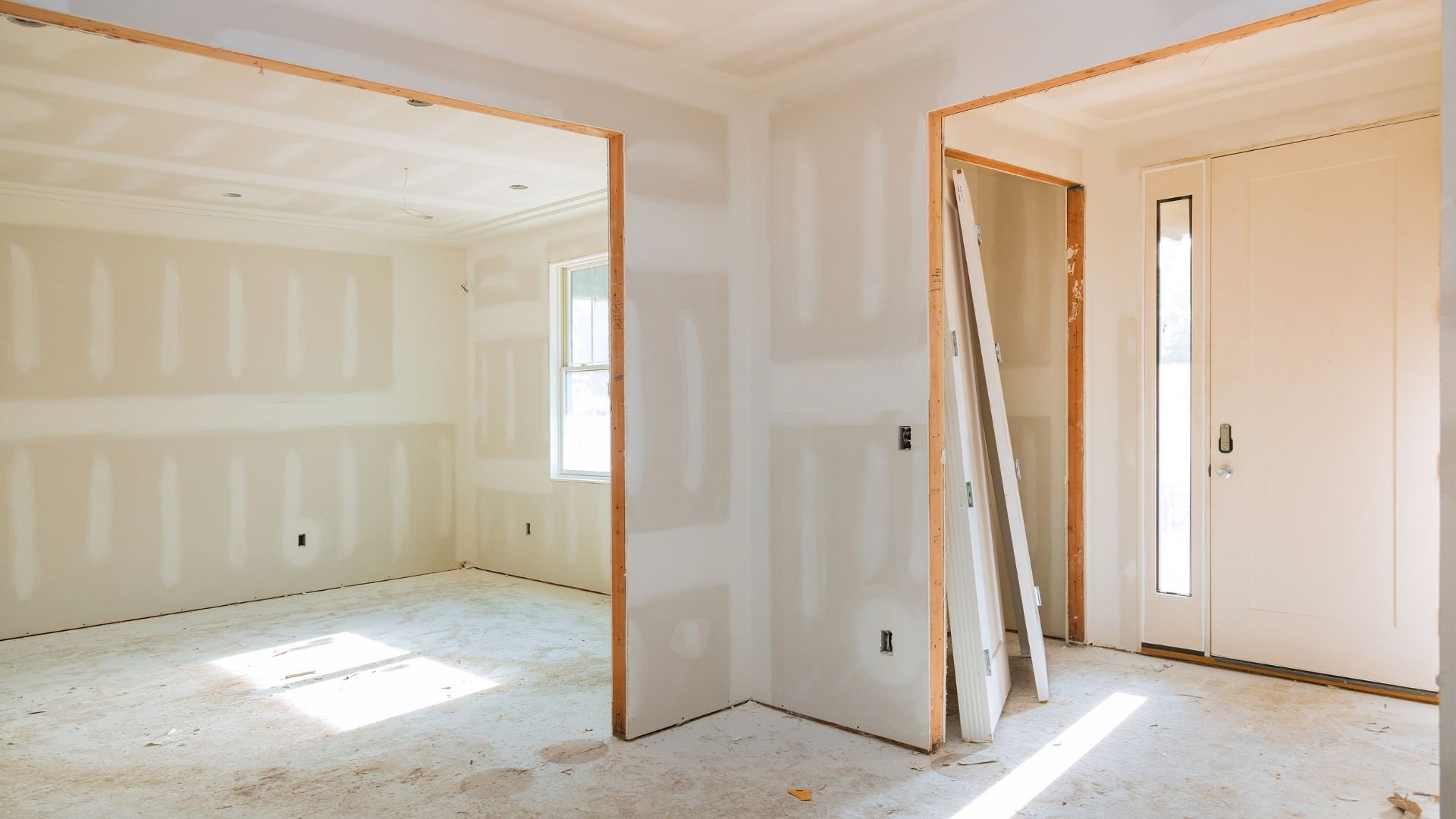 Empty room with drywall, wood trim, and white doors during home renovation