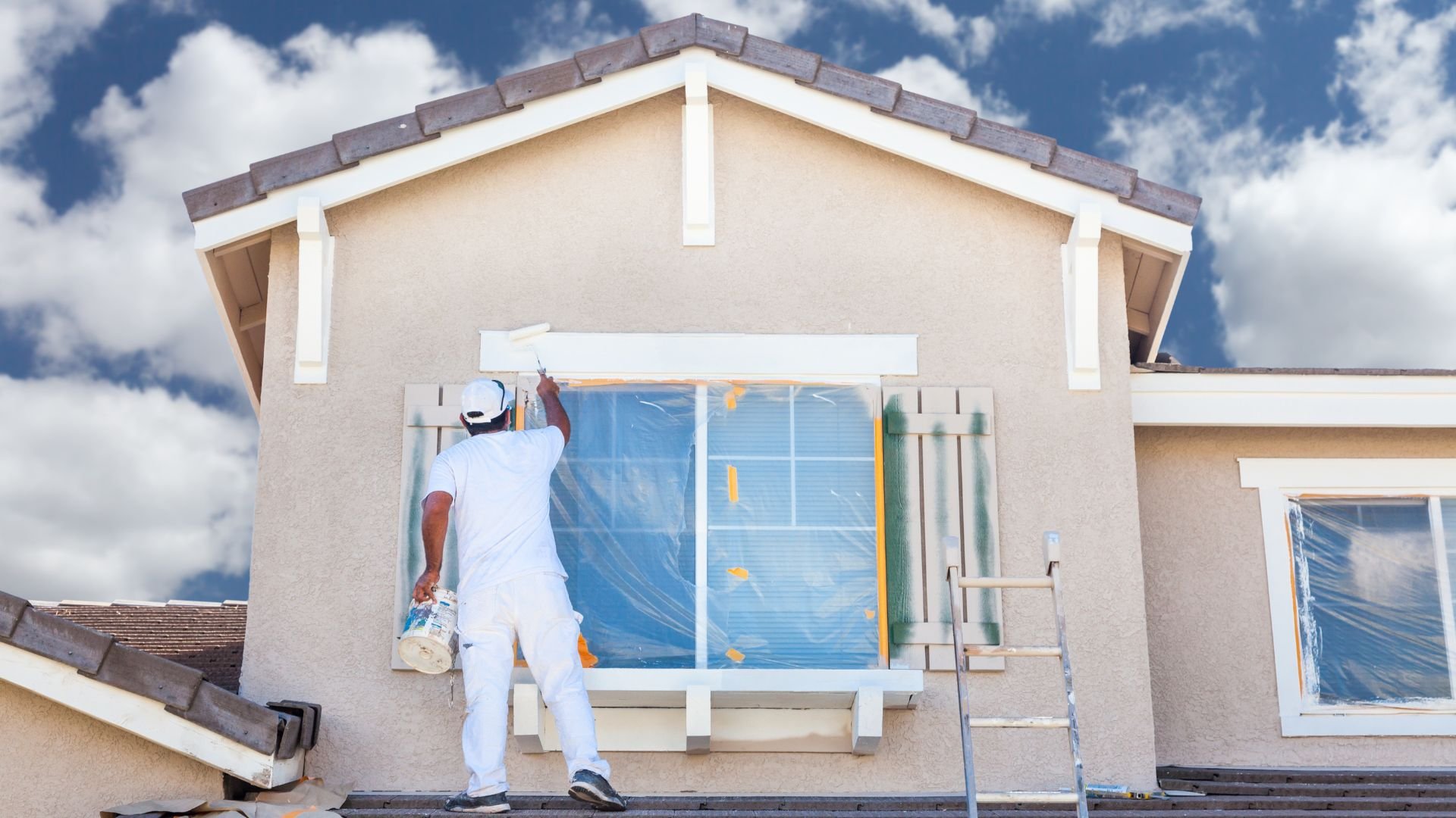 Painter in white outfit working on exterior of stucco house